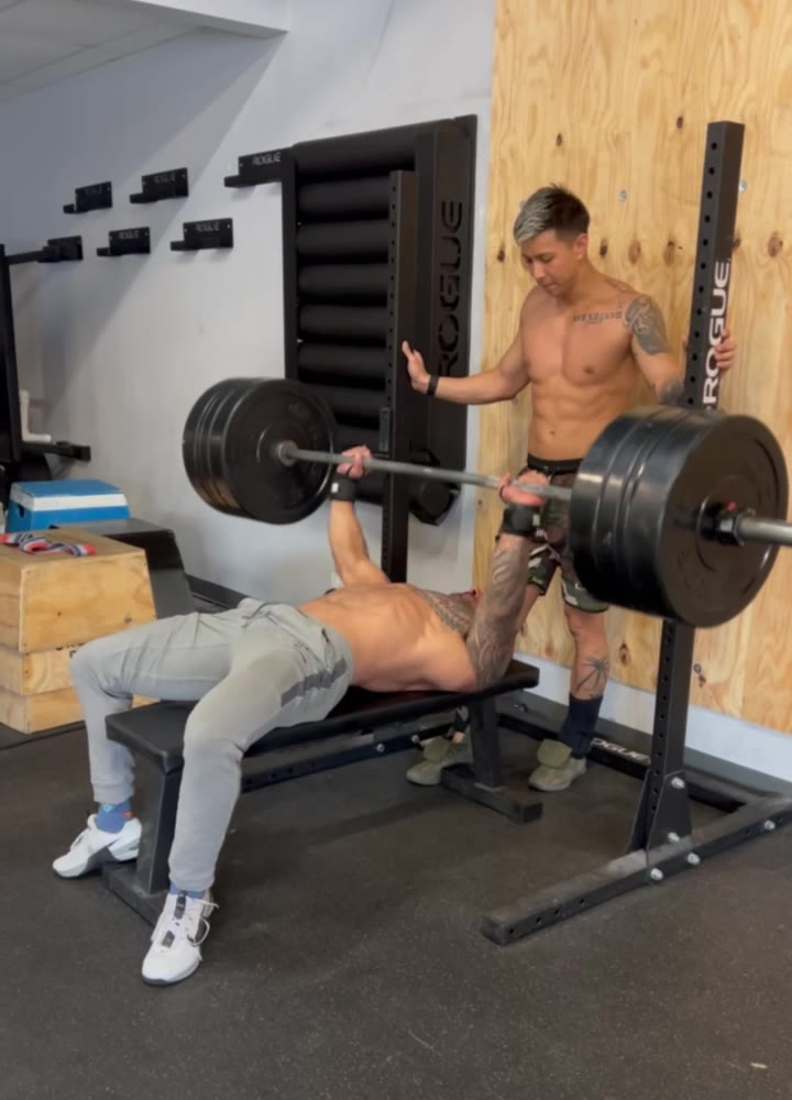 A bench press set at the gym, with a spotter standing by.
